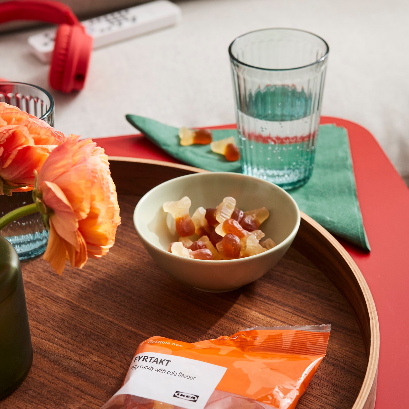 Kleine Schale mit getrockneten Früchten auf einem Holztablett, daneben ein Wasserglas, eine orangefarbene Blüte und eine Snackverpackung auf einem gedeckten Tisch.