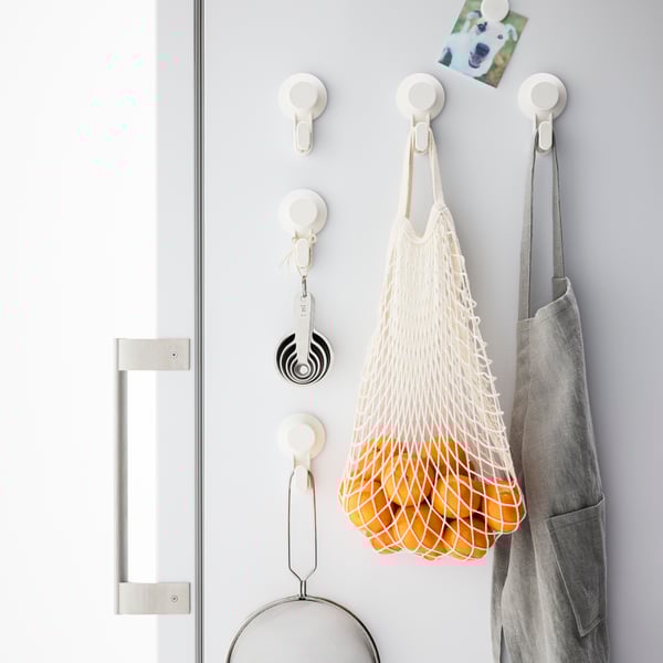 A series of TISKEN suction cups, attached to the side of a refrigerator. They hold a bag of oranges, an apron and cookware.