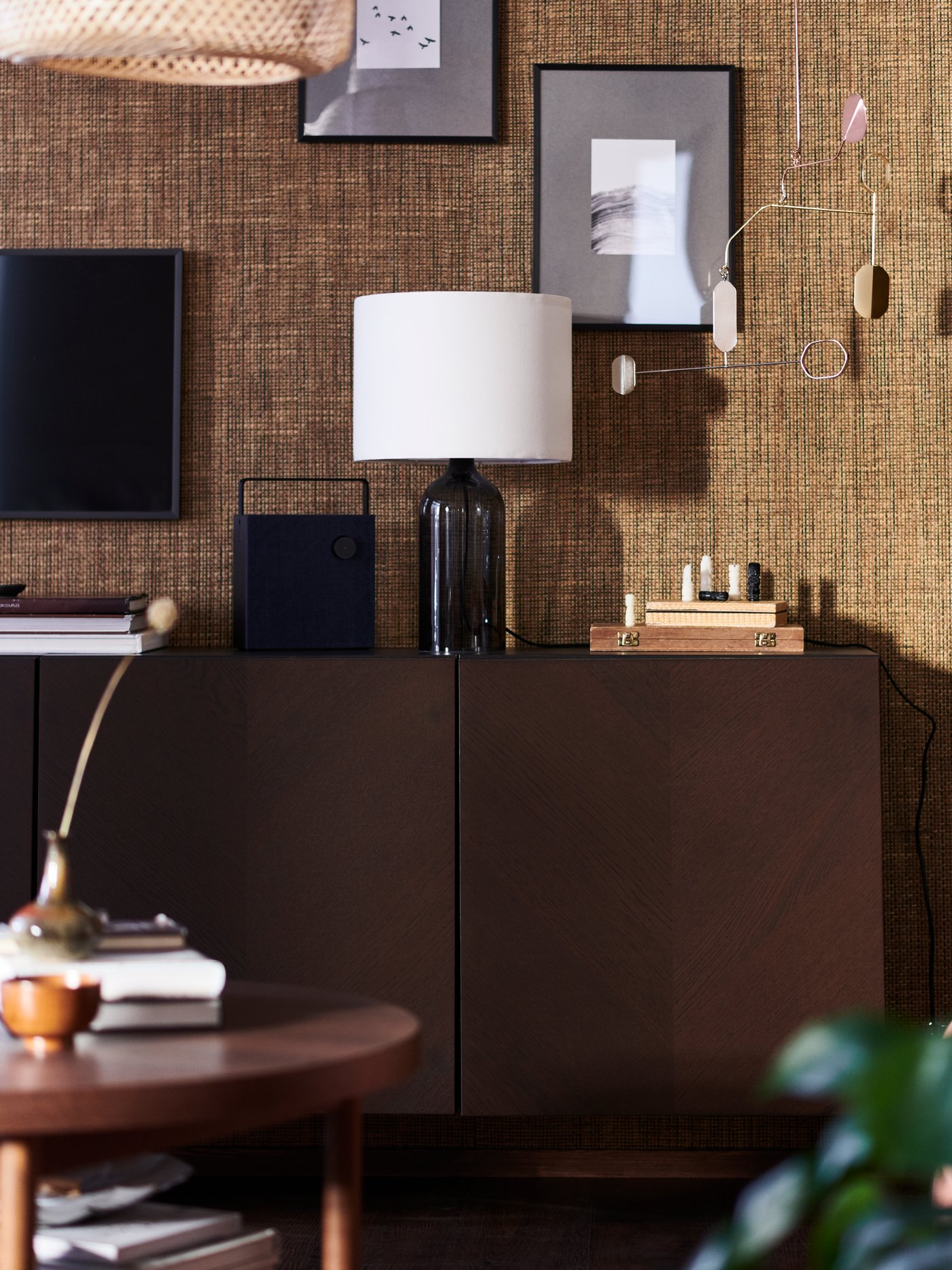 Un gabinete BESTÅ en una sala junto a una pared café claro con cuadros, una lámpara TONVIS y un altavoz Bluetooth ENEBY encima.