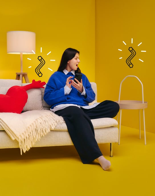 Henkilö istuu sohvalla keltaisessa huoneessa yllättynyt ilme kasvoillaa.