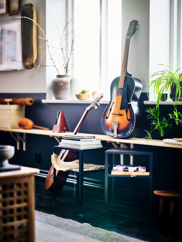 Musical instruments and magazines on TRANHULT/SANDSHULT wall shelves and a black KNARREVIK bedside table by a windowed wall.