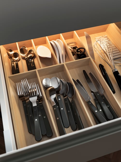Close-up of an open drawer containing a beige cutlery tray with spoons, forks, a whisk, and other cutlery items.