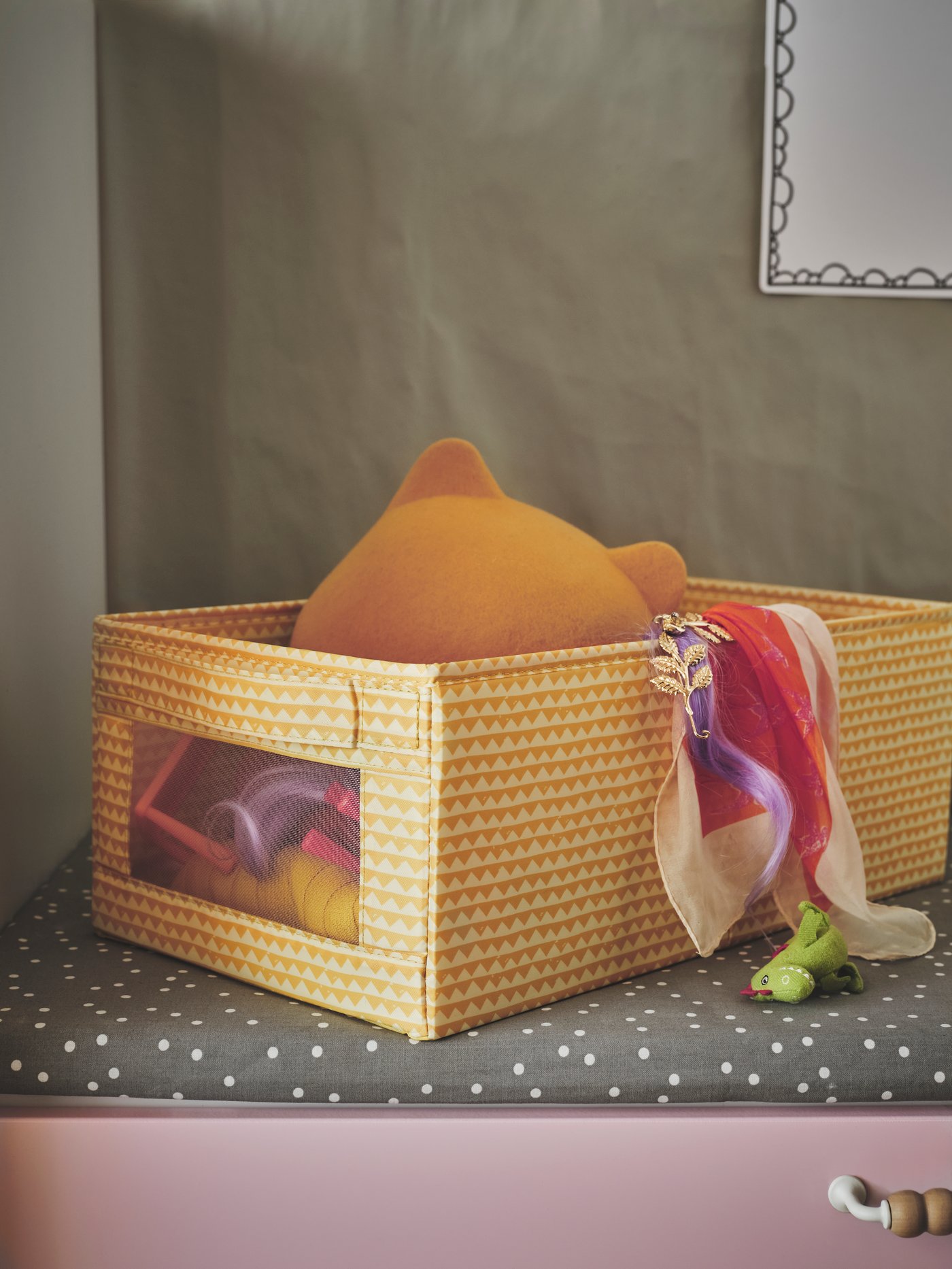 A yellow cloth box with a mesh window, full of new baby gifts including plush toys and blankets.