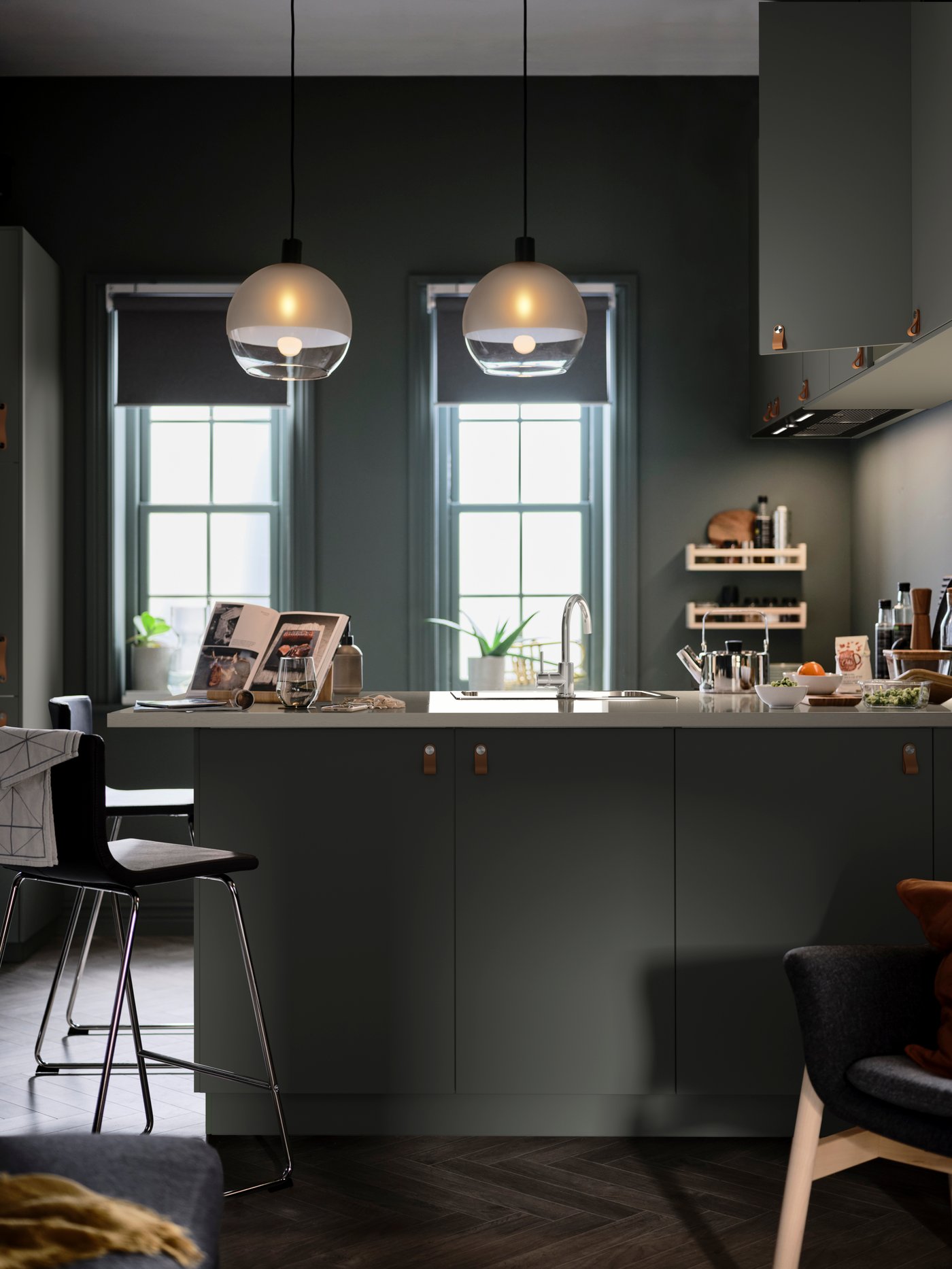 A kitchen where a worktop juts out to form a peninsula lined with BERNHARD bar stools and lit with JAKOBSBYN pendant lamps.