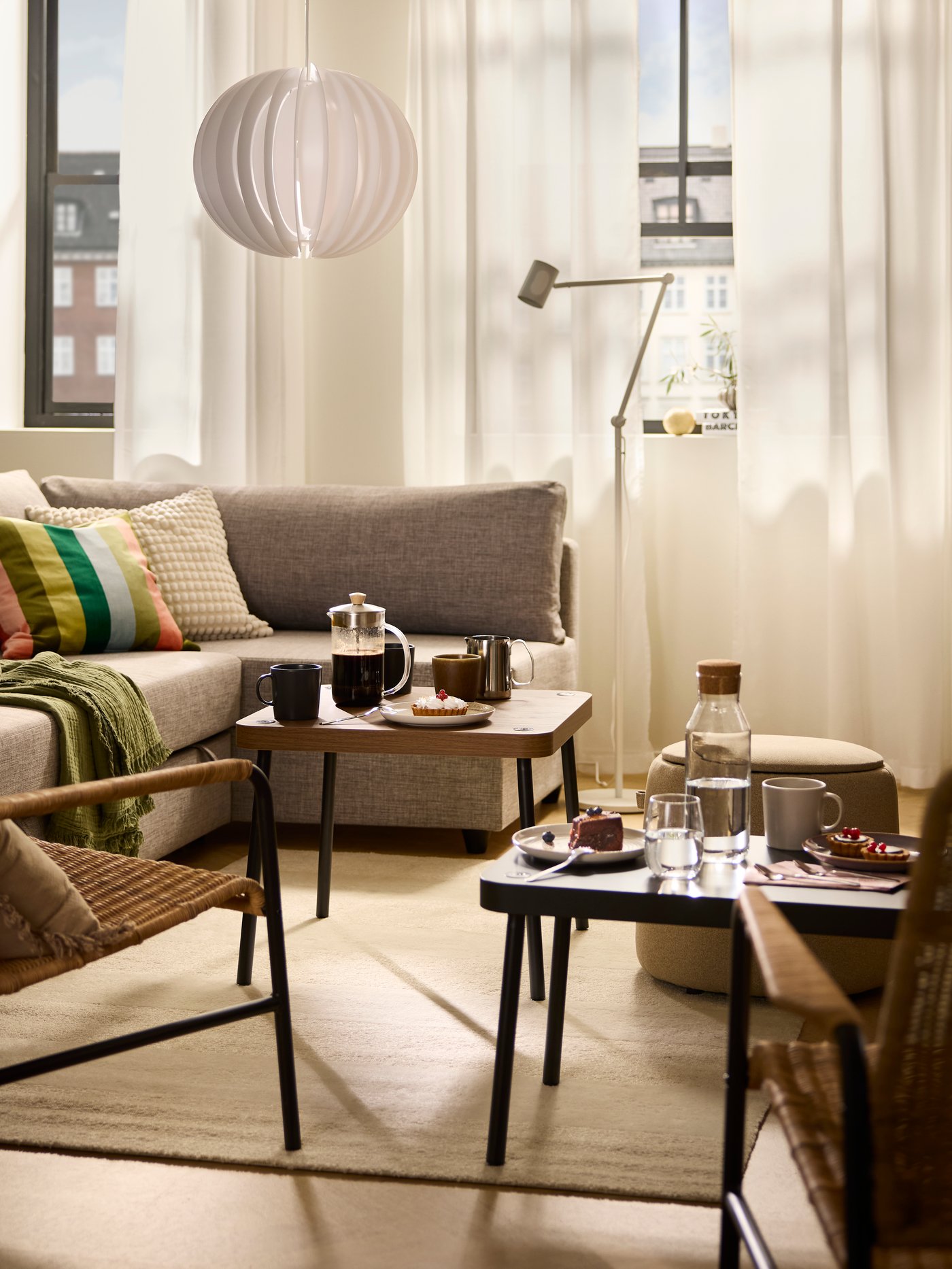 Sluncem zalitý obývací pokoj, kde mezi pohovkou a křesly ULRIKSBERG stojí stolky ze sady SONHULT s kávou a dortíky.