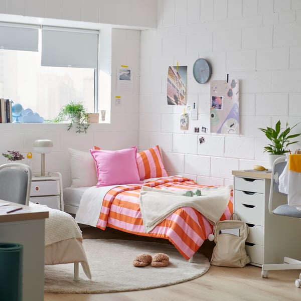 A college room with a colorful pink/orange striped comforter and posters hanging on the wall.