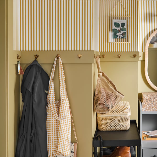 Eine gelb-weiß gestreifte Wand mit vielen kleinen messingfarbenen Haken, an denen Kleidung, Schlüssel und Accessoires hängen