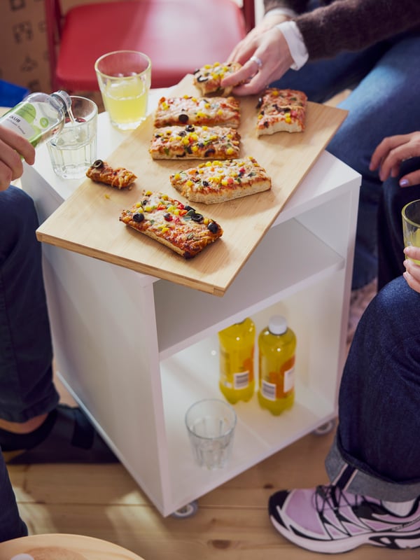 VIHALS bedside table seen from above with a cutting board on top, filled with slices of pizza. A hand grabbing a slice.