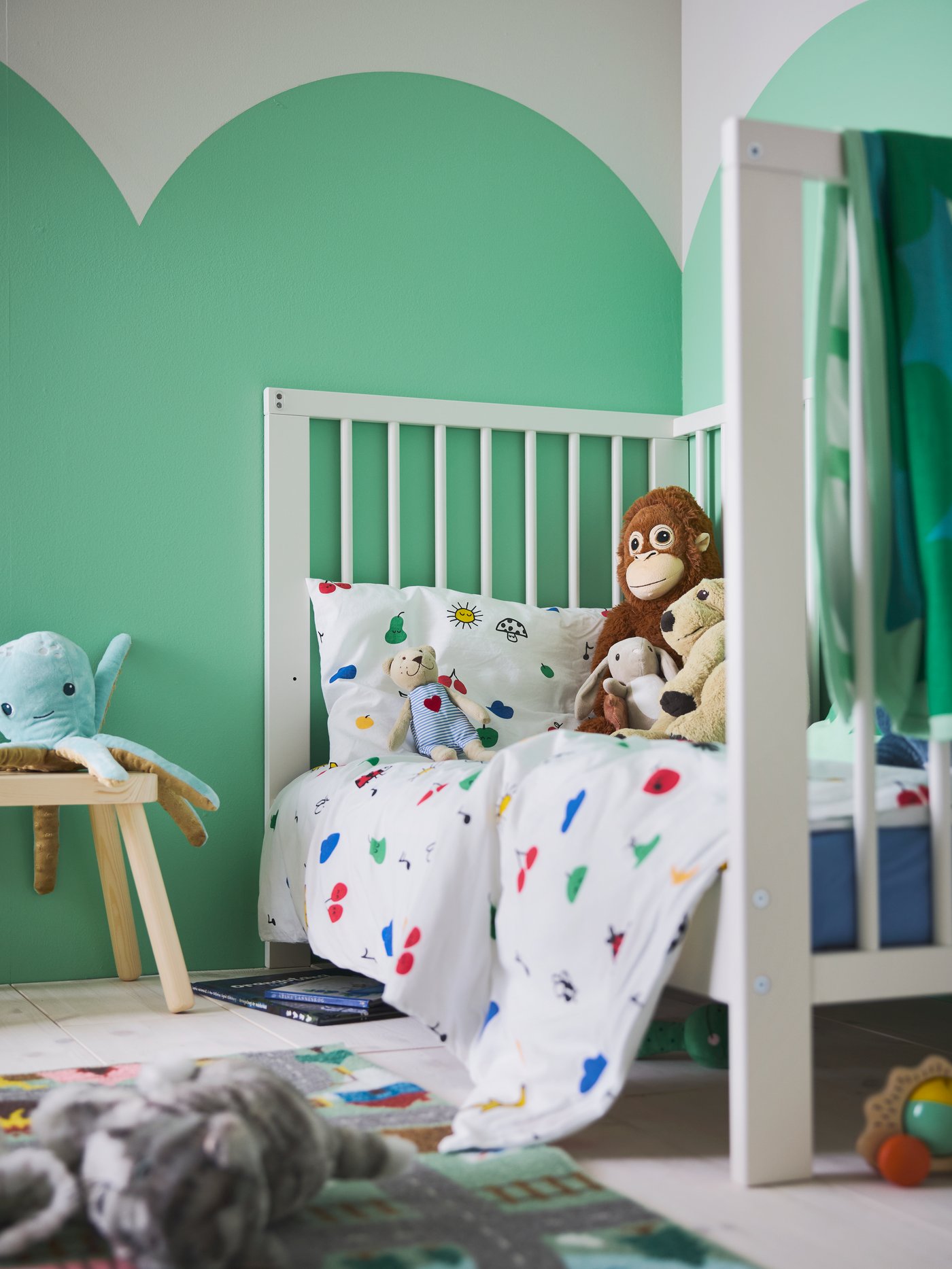 Close-up van GULLIVER ledikant opgemaakt met GRÖNFINK dekbedovertrek en kussensloop, met FLISAT kinderkrukje ernaast.