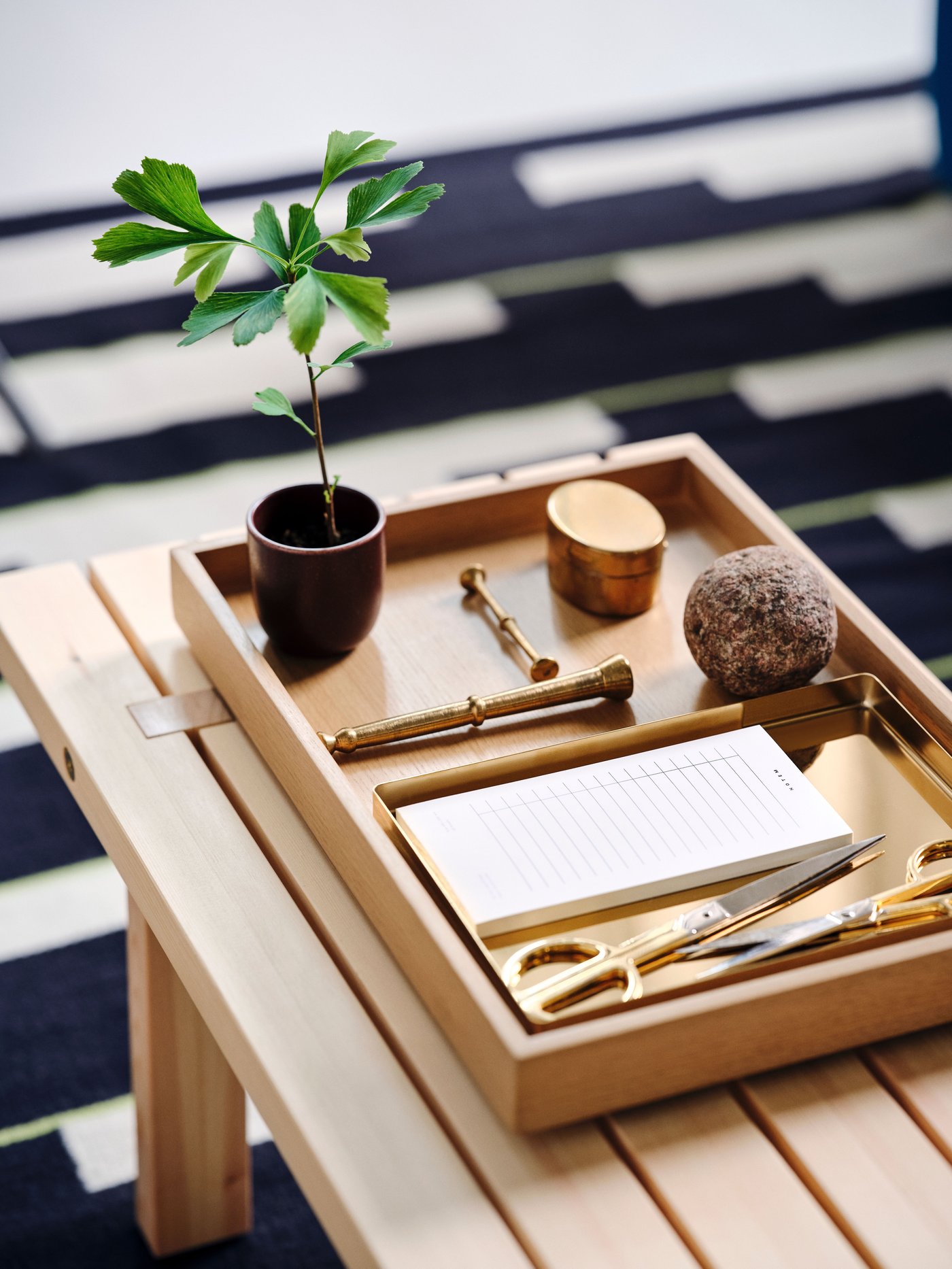 A small tray with scissors and a notebook sits on a larger STOCKHOLM 2025 tray, which in turn rests on a coffee table.