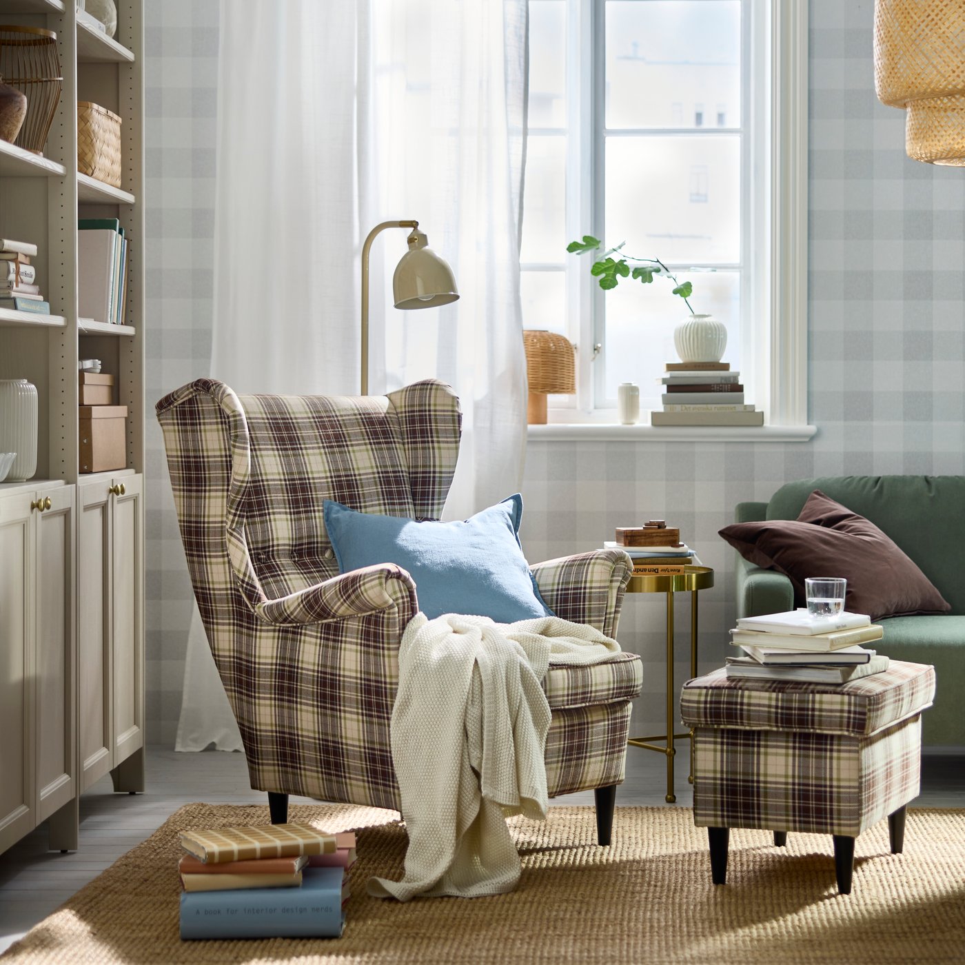 A softly sunlit living room with a tartan-pattern, beige-brown STRANDMON wing chair and footstool by a TORSJÖ side table.