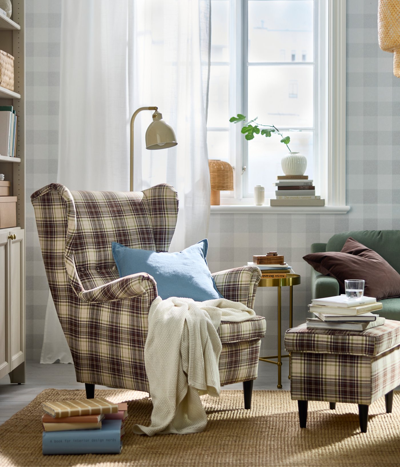 A softly sunlit living room with a tartan-pattern, beige-brown STRANDMON wing chair and footstool by a TORSJÖ side table.