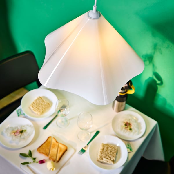 White plastic ZEBRASÄV pendant lamp hung over a dining table laid with white tablecloth and OFTAST dinnerware.