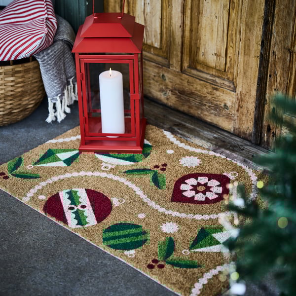 A VINTERFINT doormat in front of a wooden front door, with a red VINTERFINT lantern on top.