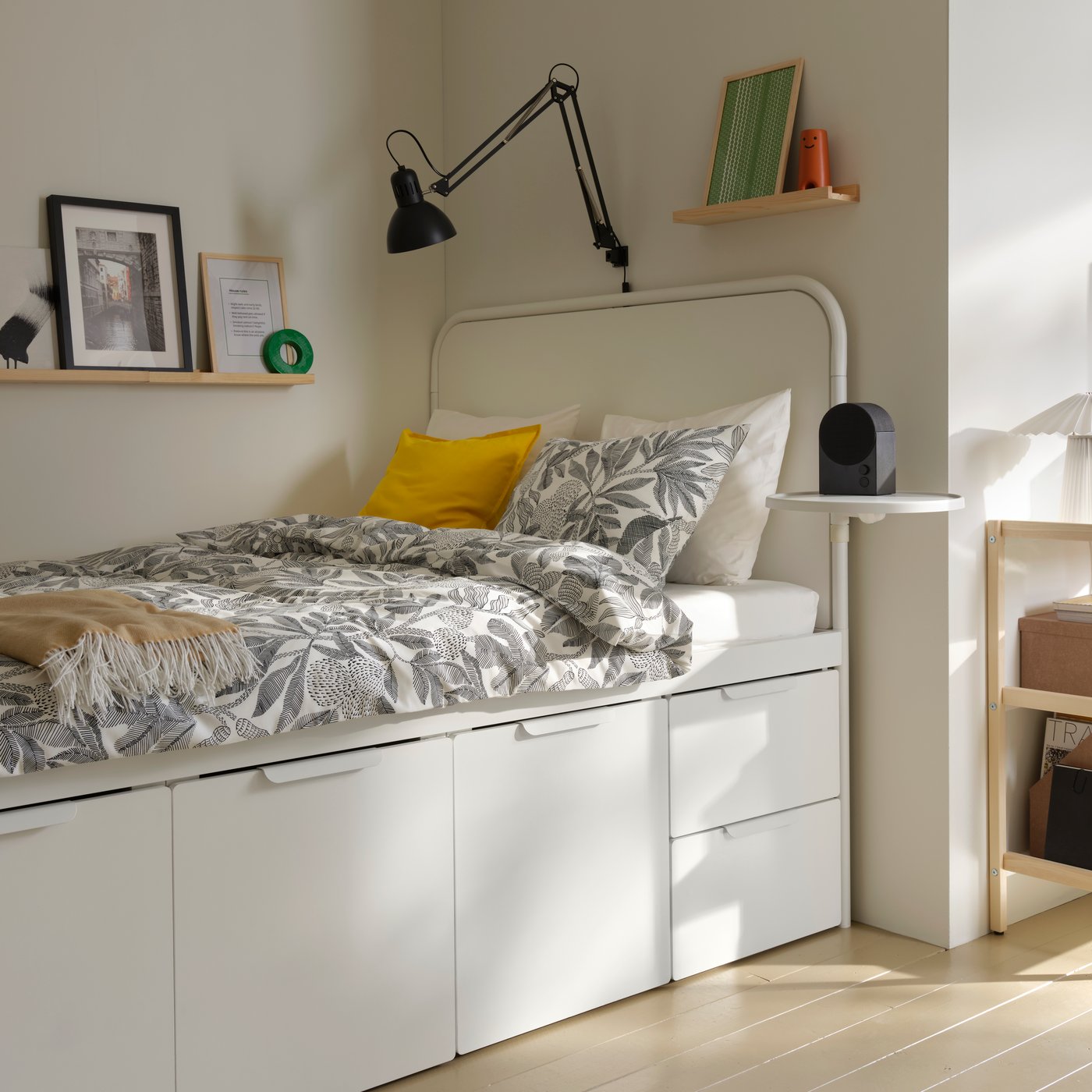 A white MÅSSKÄR bed frame with storage has a black-and-white flloral duvet, against a corner wall in a student room rental.