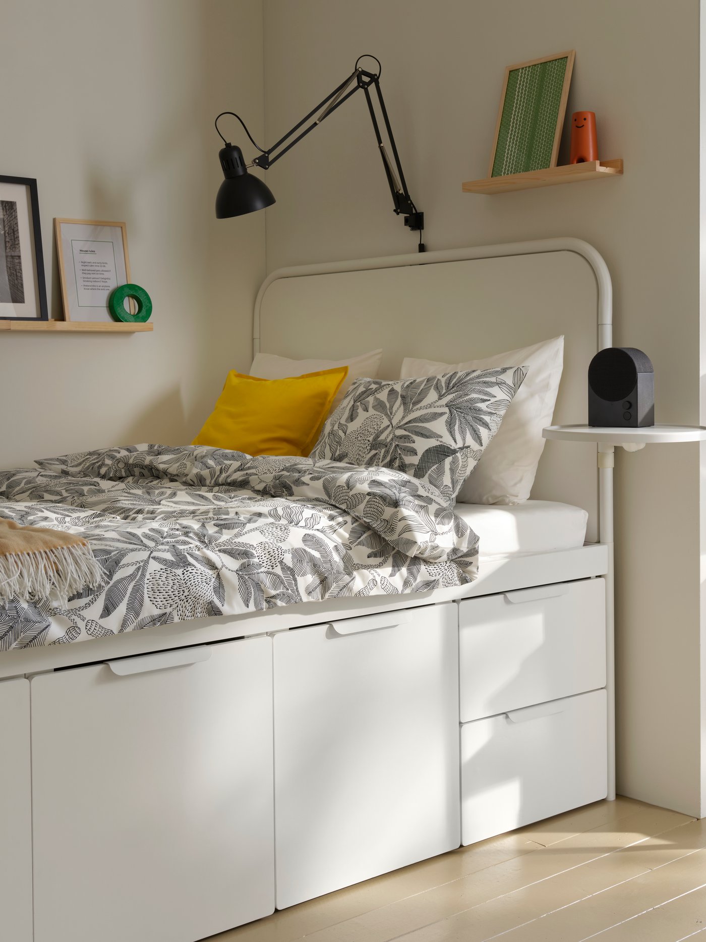 A white MÅSSKÄR bed frame with storage has a black-and-white flloral duvet, against a corner wall in a student room rental.