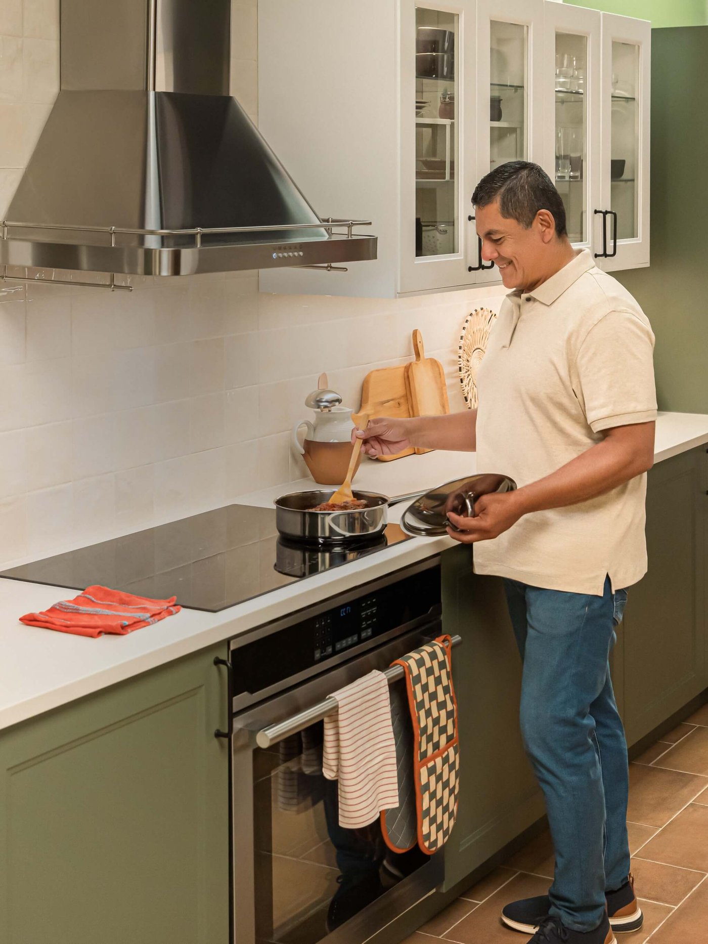 A man cooking in a modern kitchen with AXSTAD green cabinets, white countertops, and stainless steel appliances.