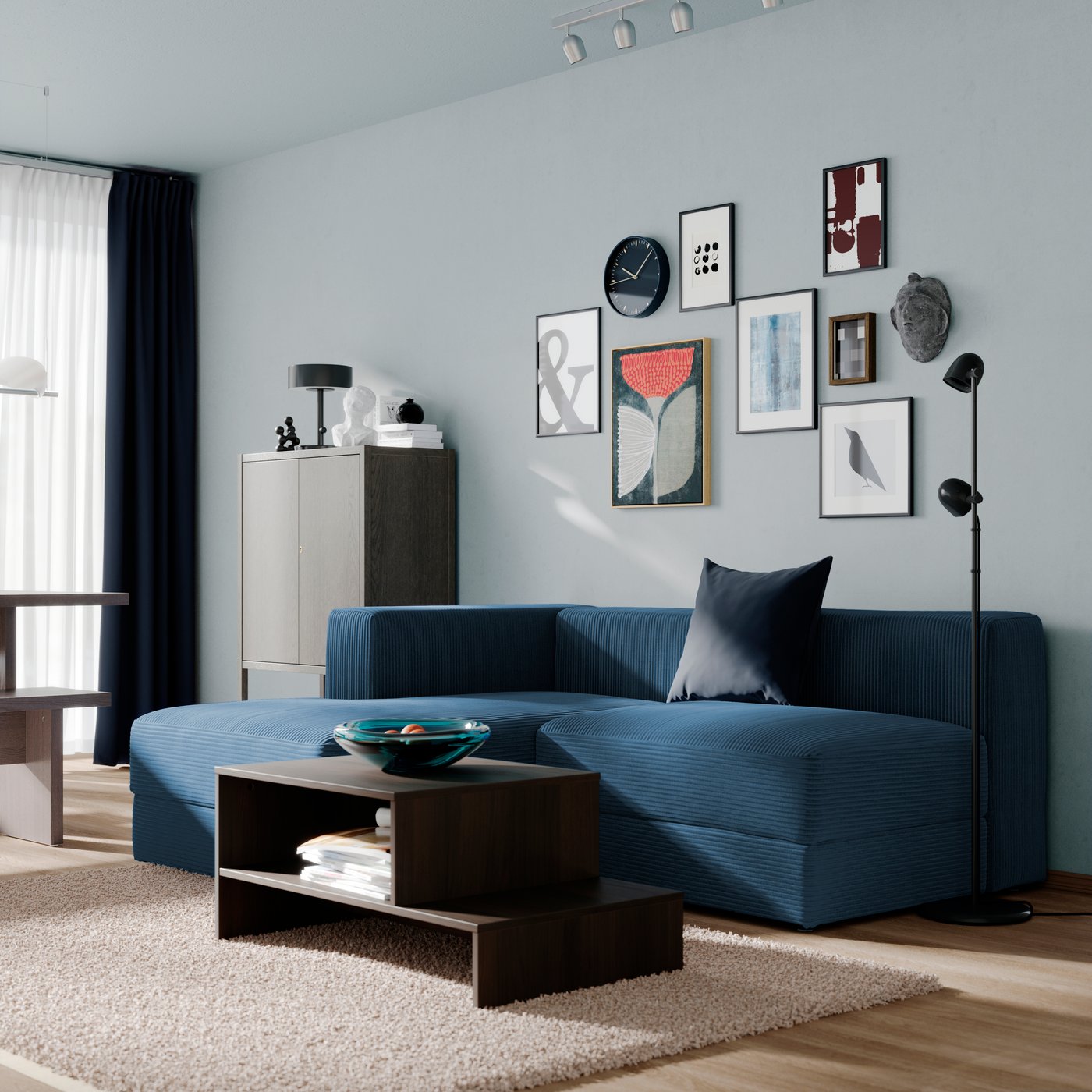 Soggiorno moderno con divano JÄTTEBO blu scuro con chaise-longue a sinistra, tavolino basso in legno scuro e parete decorata con una galleria di quadri.