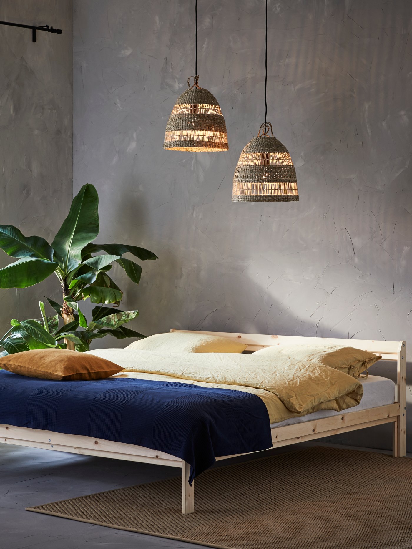 Dormitorio con dos lámparas de techo colgadas sobre una estructura de cama con colcha azul, una maceta y una alfombra lisa en el suelo.