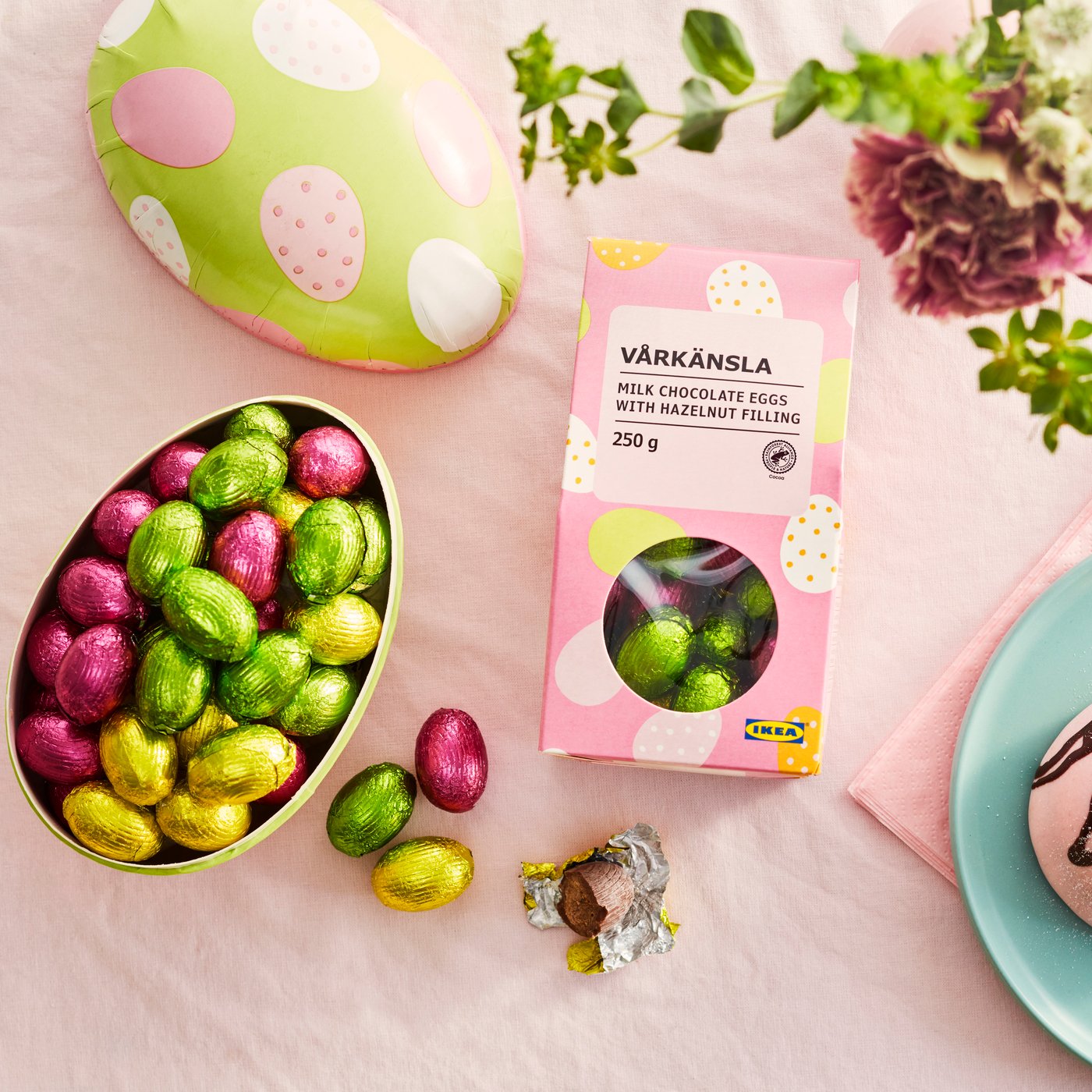 Rainforest Alliance-certifierade VÅRKÄNSLA mjölkchokladägg med hasselnötsfyllning som ligger i ett påskägg på ett bord med rosa duk. 