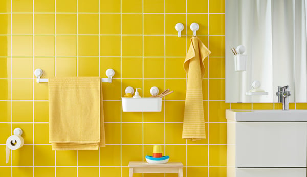 Bright yellow-tiled bathroom with white TISKEN towel rack, basket and hooks all mounted to wall with suction cups.