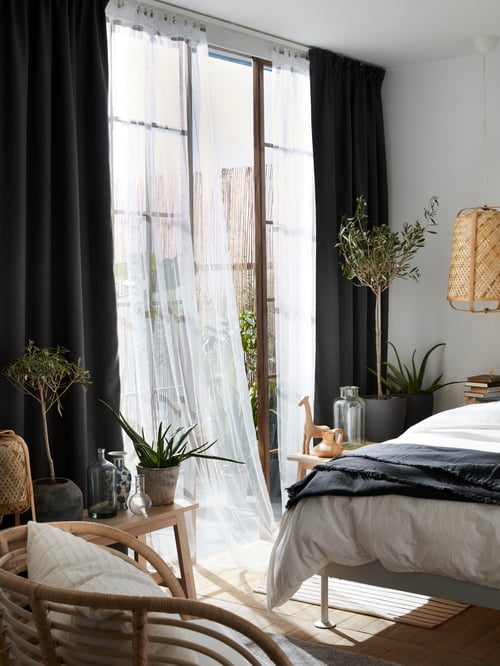 A light-filled bedroom with large glass doors behind flowy, white LILL net curtains layered under thick darkening curtains.