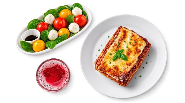 Lasagne gratinée servie avec une salade caprese composée de tomates cerises, mozzarella et basilic, accompagnée d’une boisson rouge.