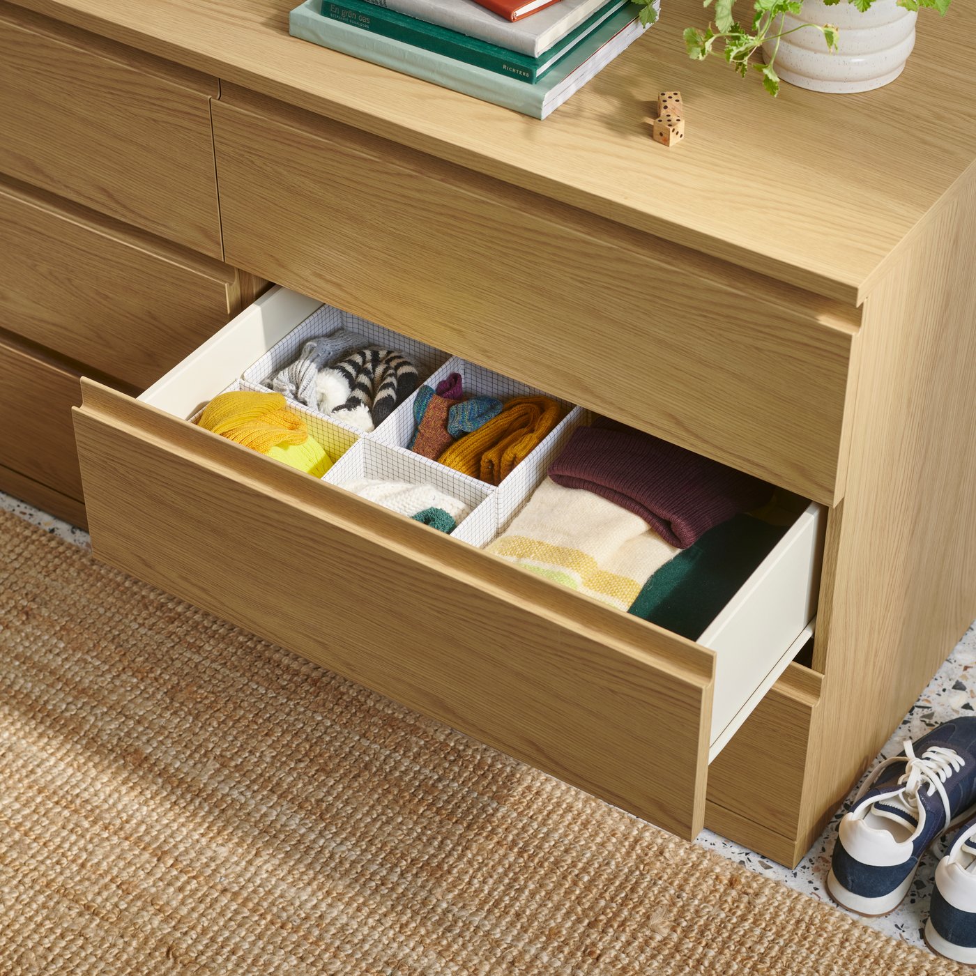 STORKLINTA chest of drawers in oak effect with one drawer open showing neatly organised items inside.