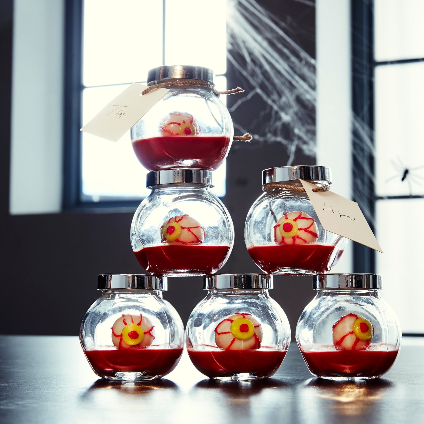 Ein Stapel kleiner Glasgefäße, gefüllt mit roter Gelatine und Leckereien, die wie Augäpfel aussehen.