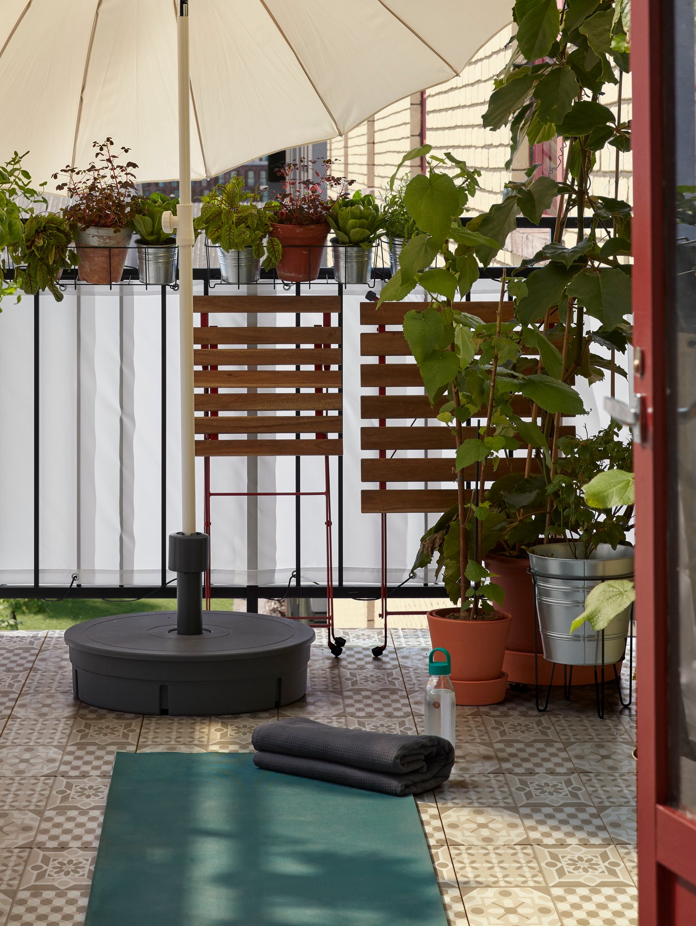 Una mesa y una silla están dobladas y apartadas para dejar espacio para una estera de yoga que está en el suelo de un balcón.
