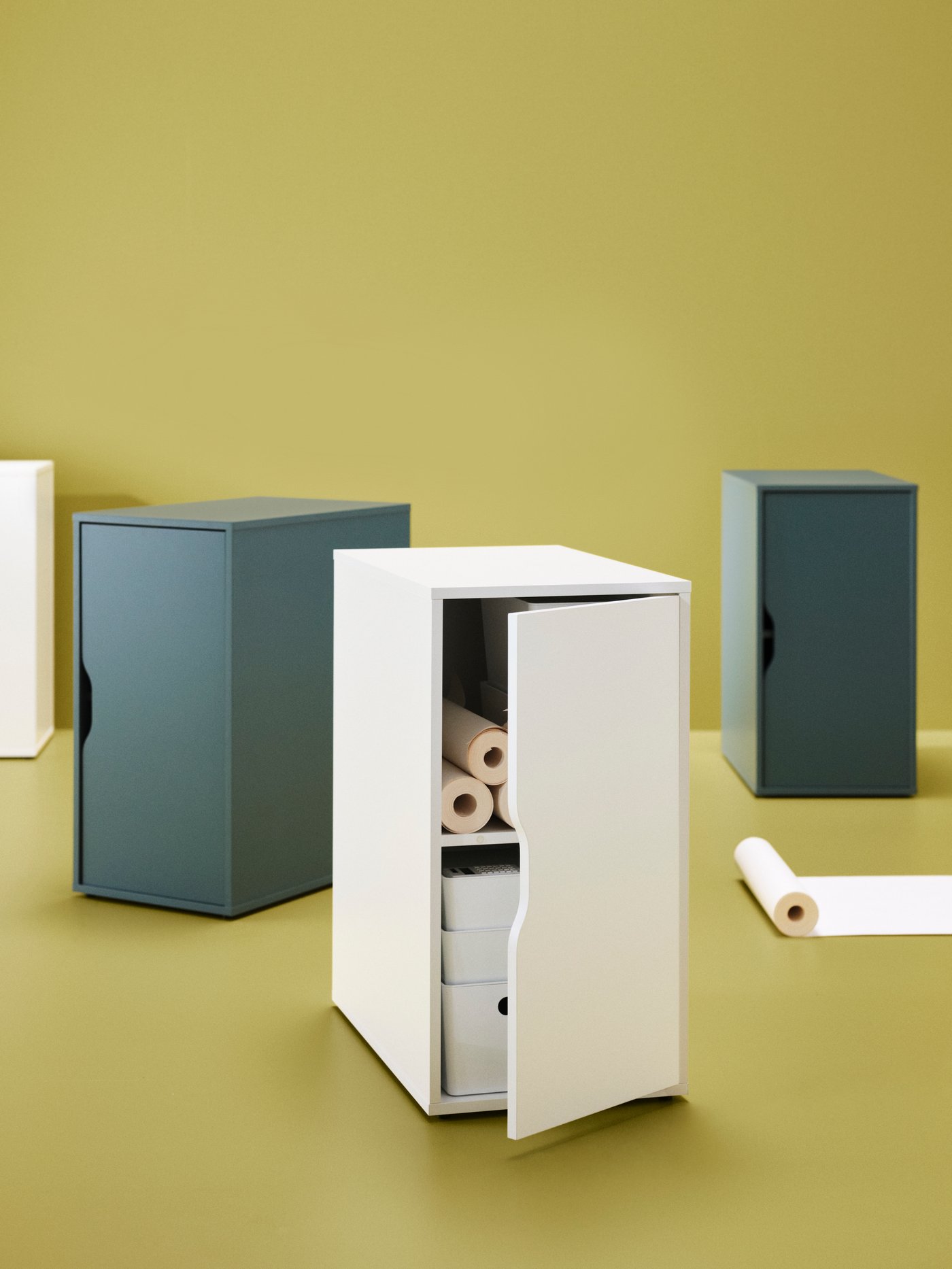 Una imagen de fondo amarillo con cuatro cajoneras ALEX con puerta. Dos de ellas son blancas y otras turquesas, en una de ellas la puerta está abierta mostrando el espacio interior.