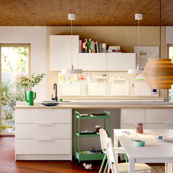 Kitchen storage with VEDDINGE white doors and drawer fronts, SKÅDIS pegboards on the wall, and a ceiling lamp hanging.