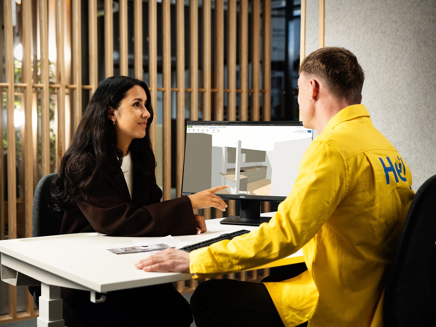 Two people discussing a kitchen design at a desk in a modern office setting.