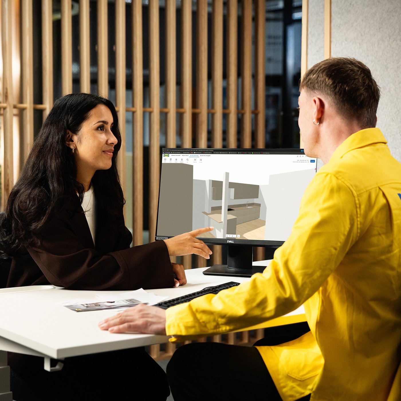 An IKEA employee and a customer looking at a kitchen 3D layout on a monitor.