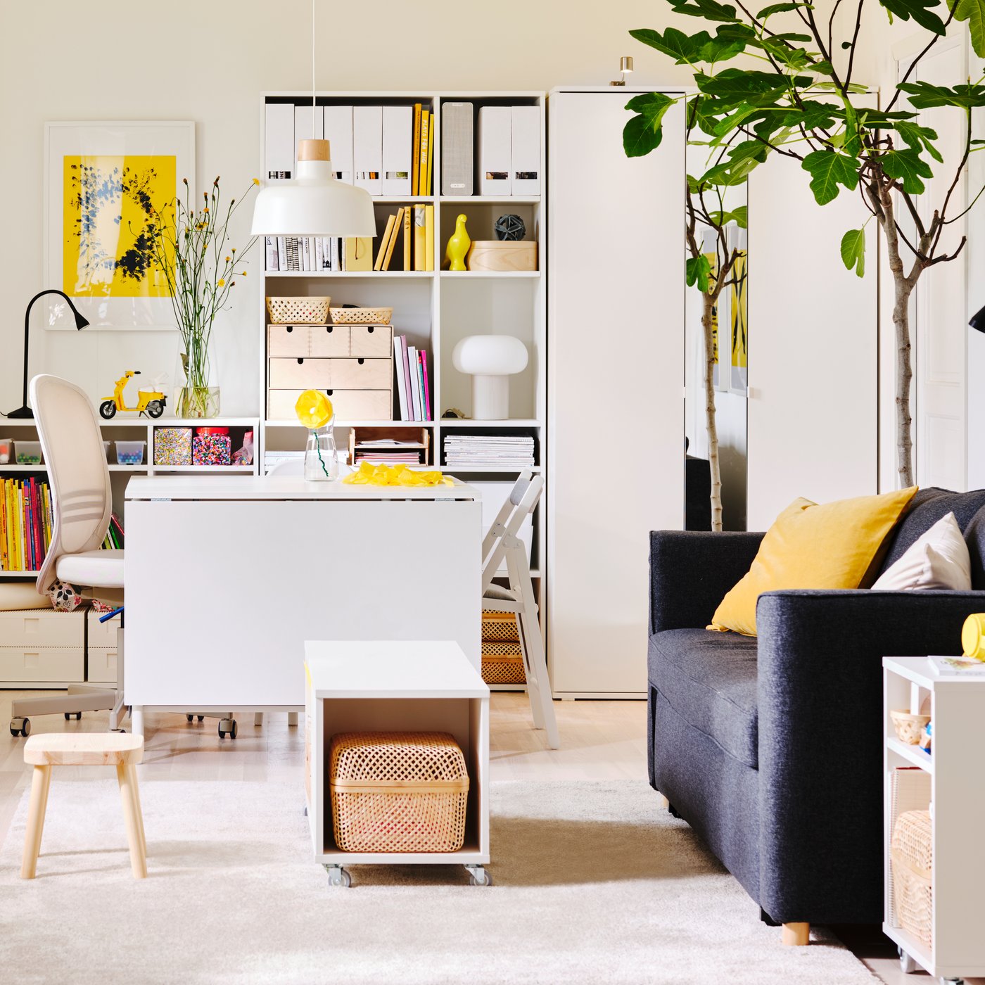 Soggiorno bianco e giallo con mobili bianchi e un divano letto PÄRUP grigio scuro. Sul pavimento ci sono giocattoli per bambini.