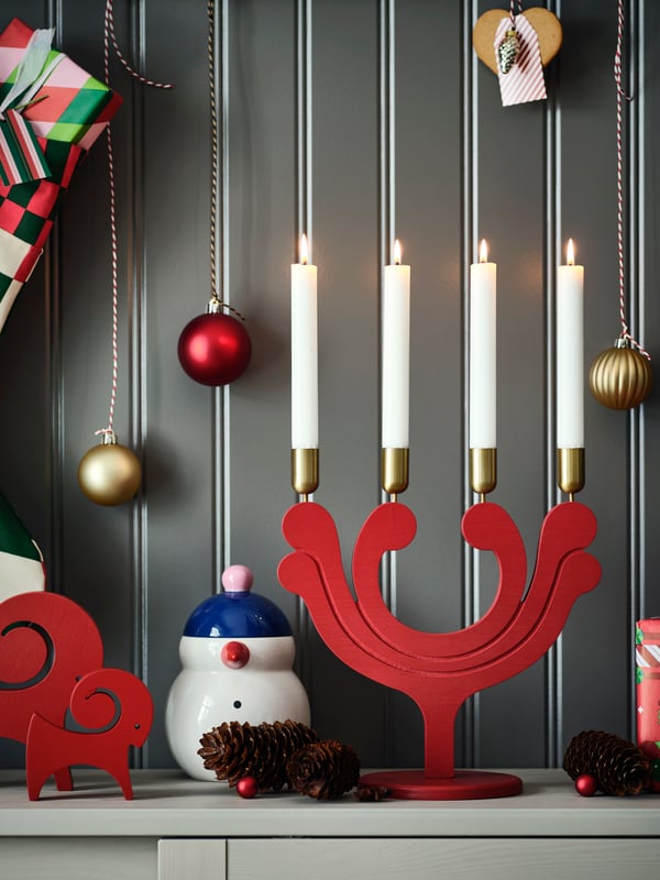 Weihnachtliche Deko mit Kerzen, Rentierfigur, Schneemann und Geschenken vor grauer Wand.