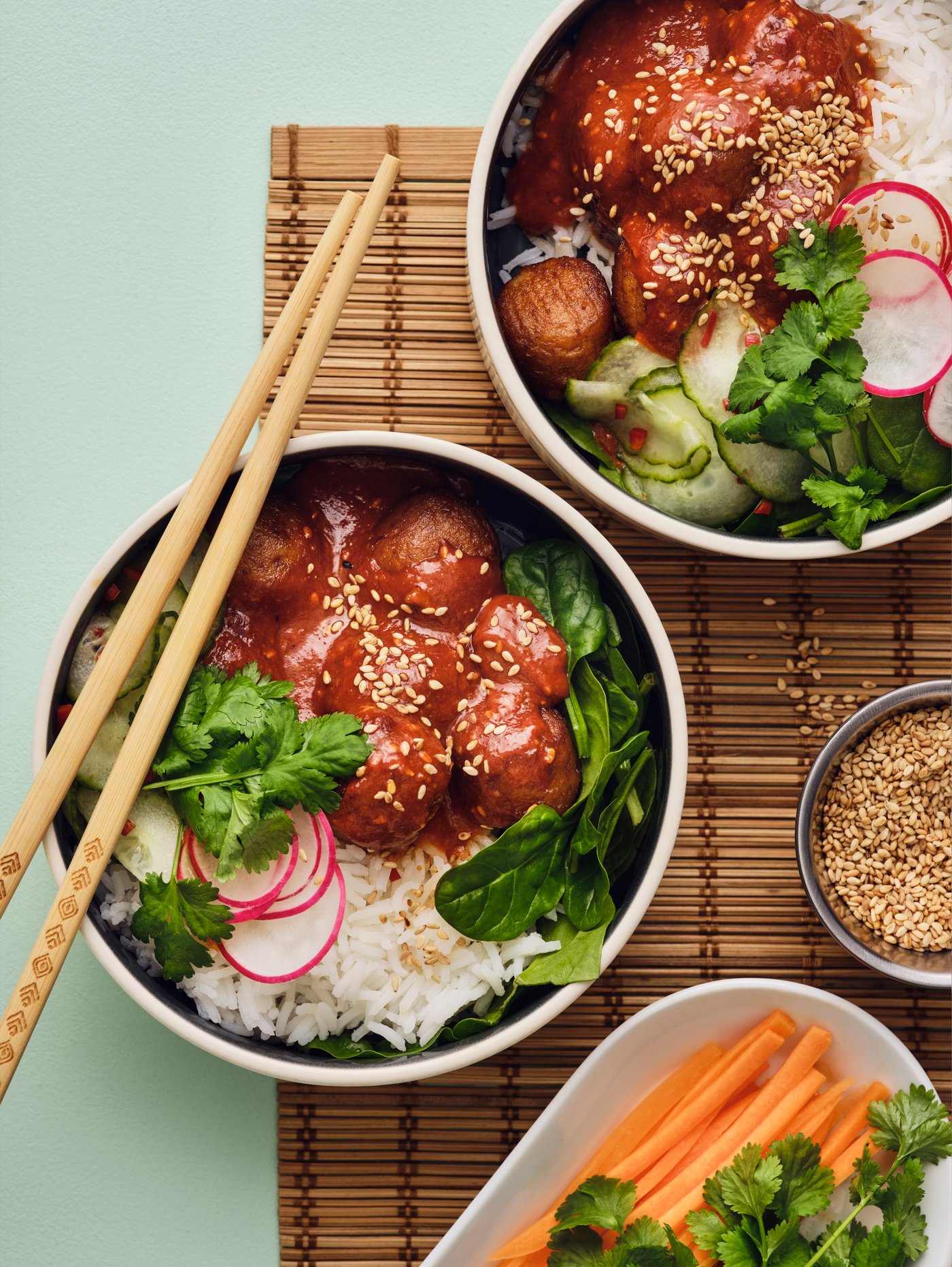 Two white bowls are placed on a light green table, and they are filled with a salad made of plant balls, rice and vegetables.