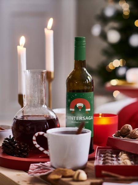 Eine Flasche VINTERSAGA Glühwein steht auf einem weihnachtlich geschmückten Tisch mit Kerzen und Nüssen.