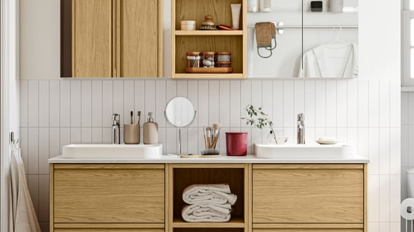 A white-tiled bathroom has ÄNGSJÖN bathroom furniture in oak effect, including a wash-stand with drawers and wall cabinets.
