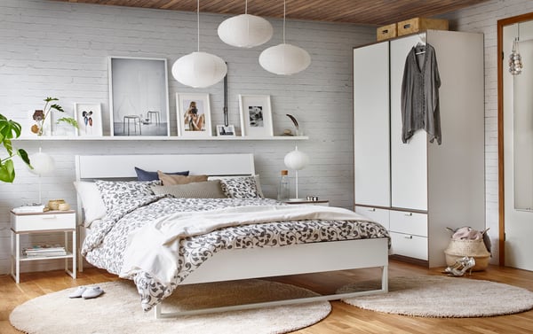 Ein Schlafzimmer in weiß mit Bett, Nachttisch und Kleiderschrank.