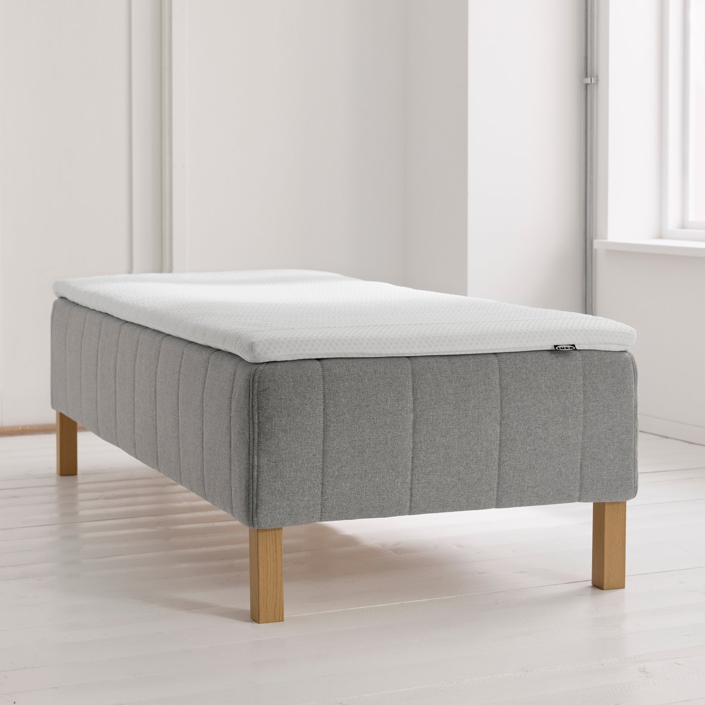 En RÅHOLMAR resårmadrassbotten står på det vita golvet i ett rum med vita väggar.
