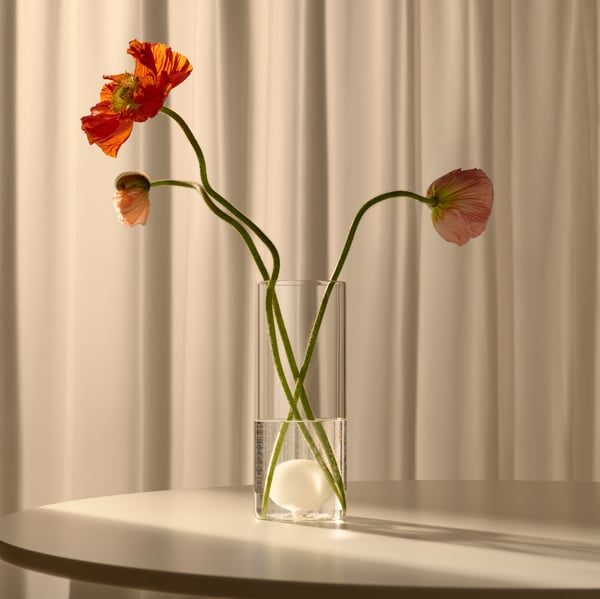 A pair of hands holds up the lid of an orange VARMBLIXT glass doughnut-shaped bowl above a table with sketches of the object.