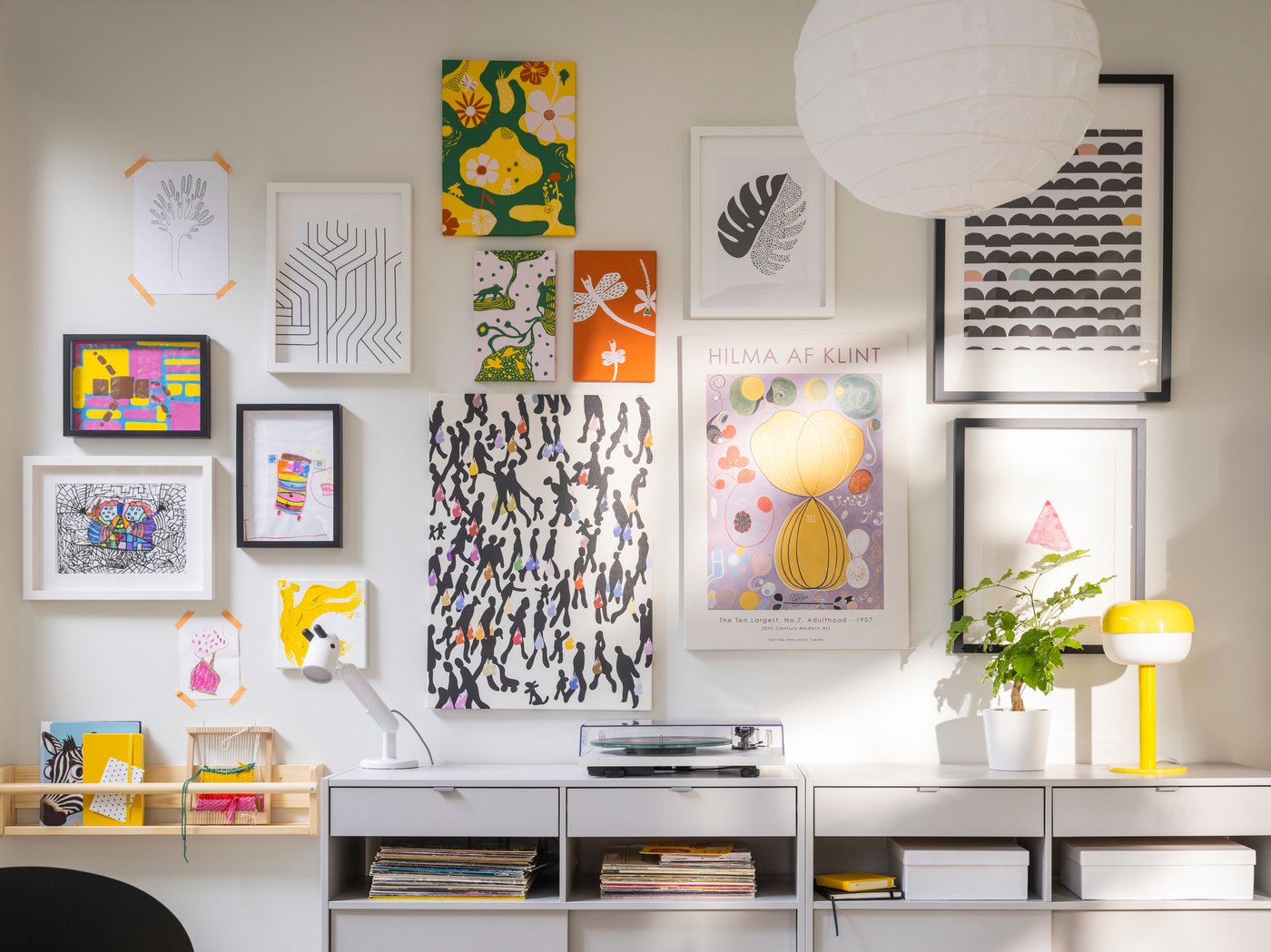 Una stanza bianca e luminosa con una parete ricoperta di immagini in varie cornici RÖDALM, appese sopra buffet SPIKSMED grigio chiaro.