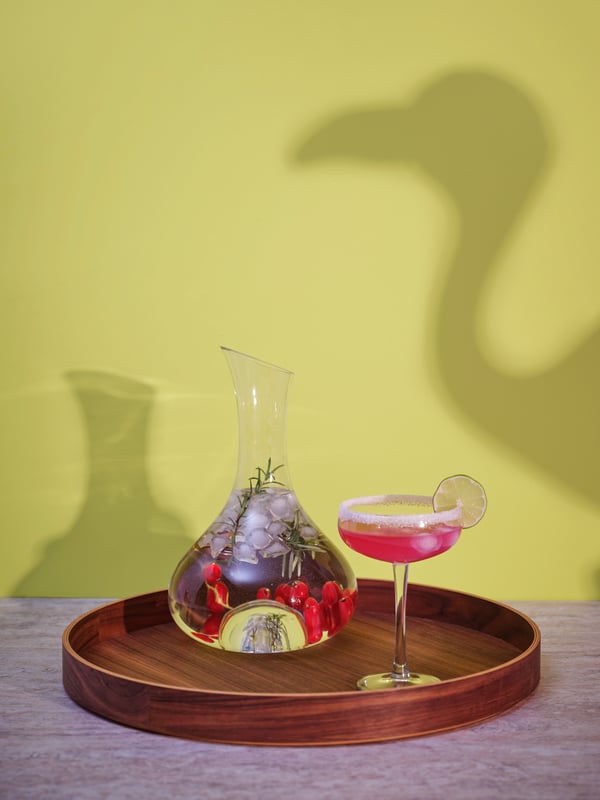 En bricka framför en gul vägg. på brickan står en karaff och en champagnecoupe.