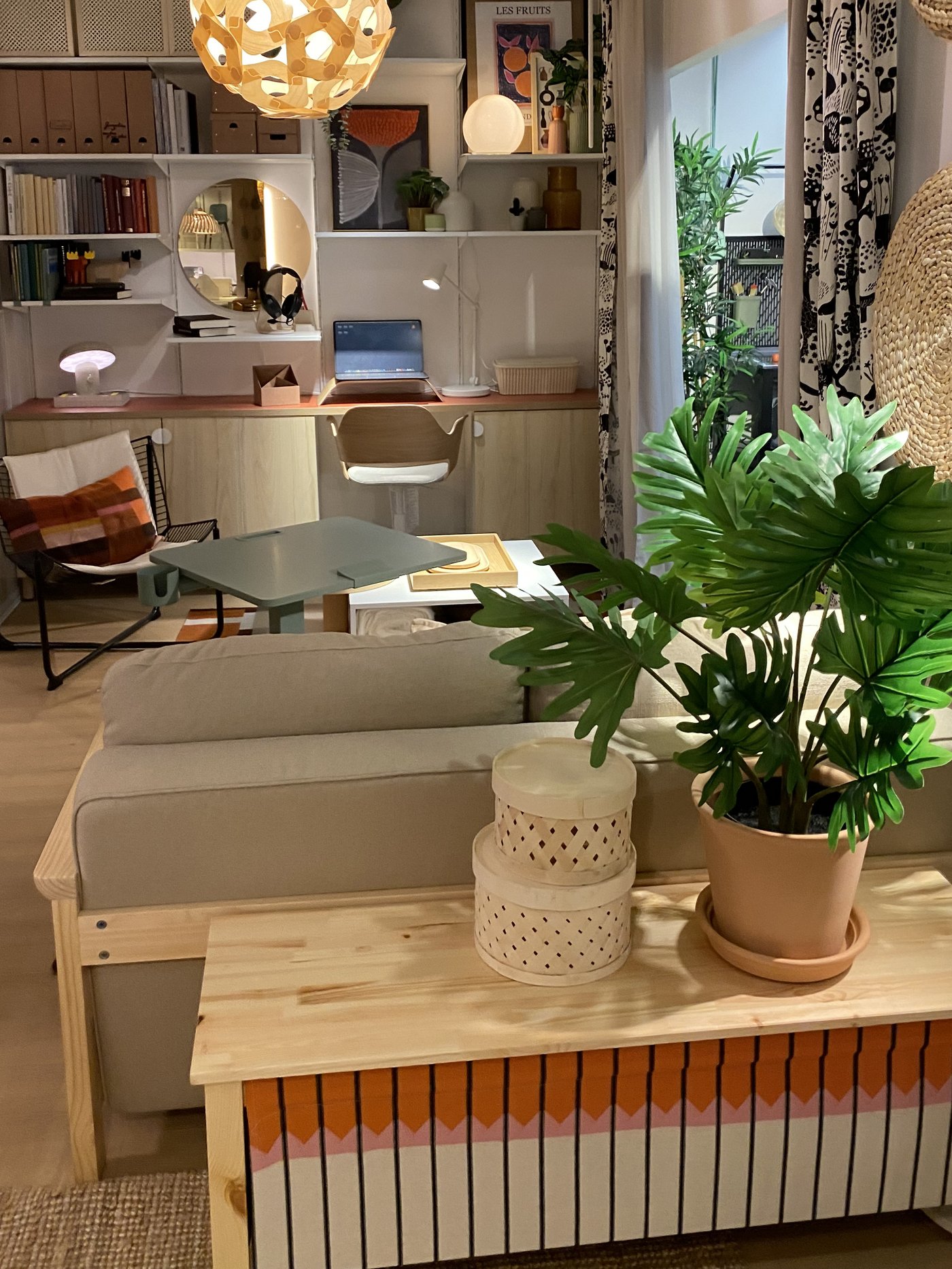 Un salon avec lumières tamisées, un canapé gris et bois, un meuble avec des plantes dessus et étagères murales.