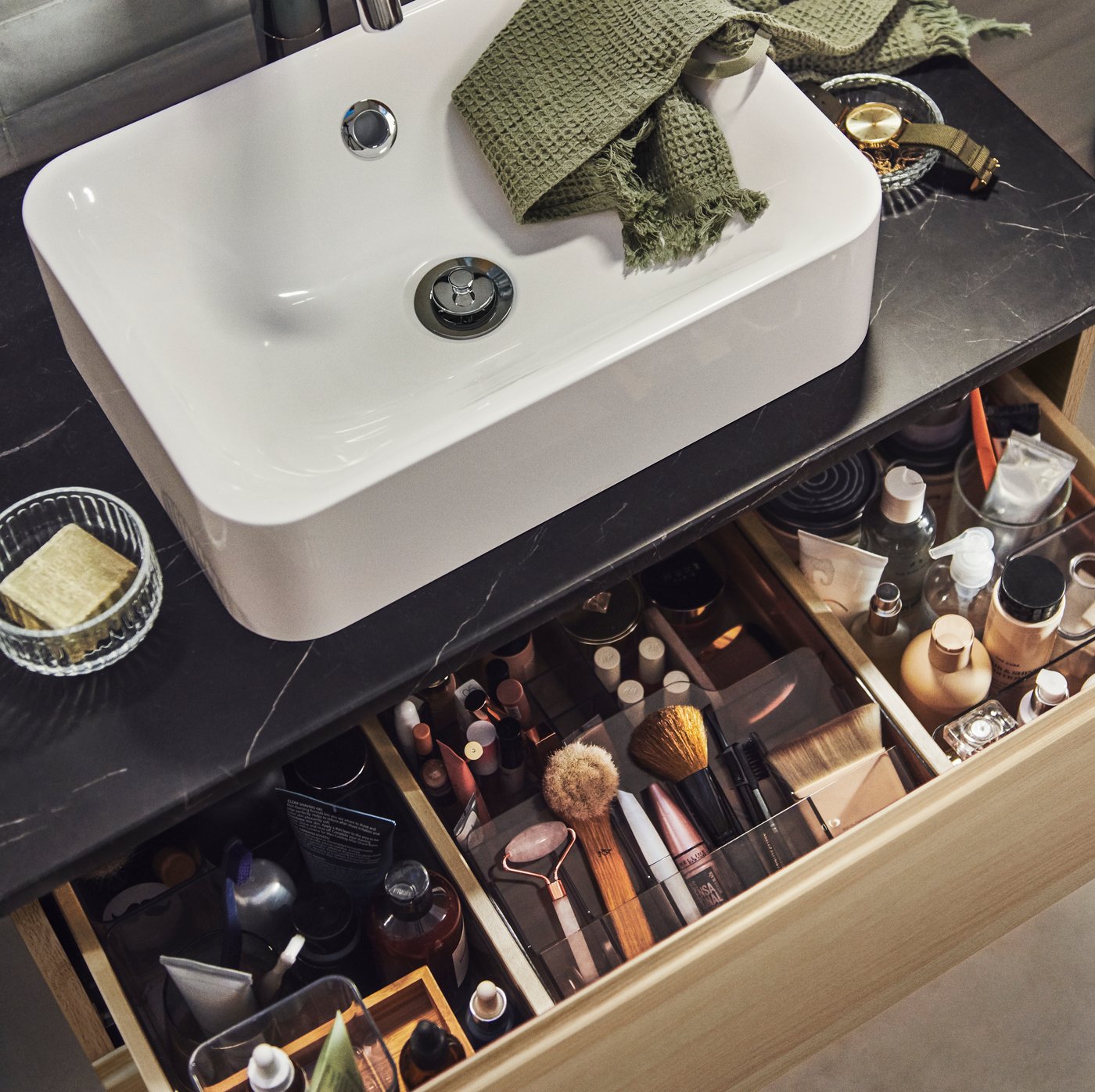 כיור HÖRVIK מעל ארונית כיור שאחת המגירות שלה פתוחה ובתוכה אביזרים ומוצרי איפור מסודרים.