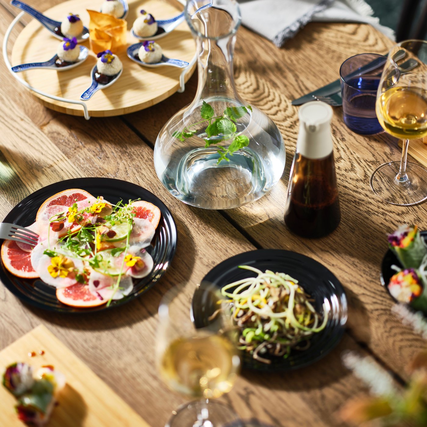 Une table MÖRBYLÅNGA en placage de chêne foncé est dressée avec des assiettes de différentes couleurs, des plats de fête et une carafe STORSINT.