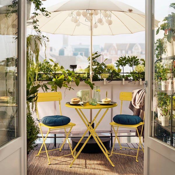 IKEA SUNDSÖ yellow table with 2 chairs on a balcony with IKEA HÖGÖN parasol.