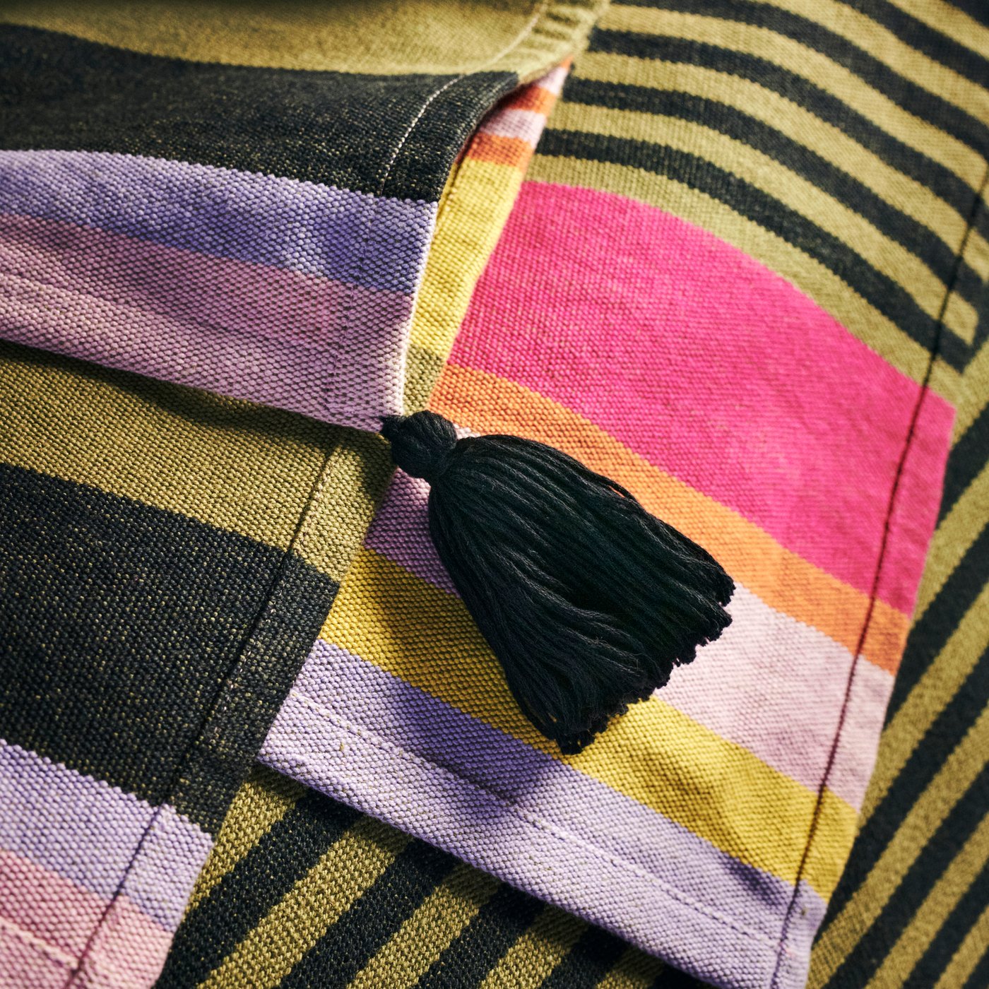 Detalle de la cobija de rayas MÄVINN de colores con una borla negra hecha a mano.