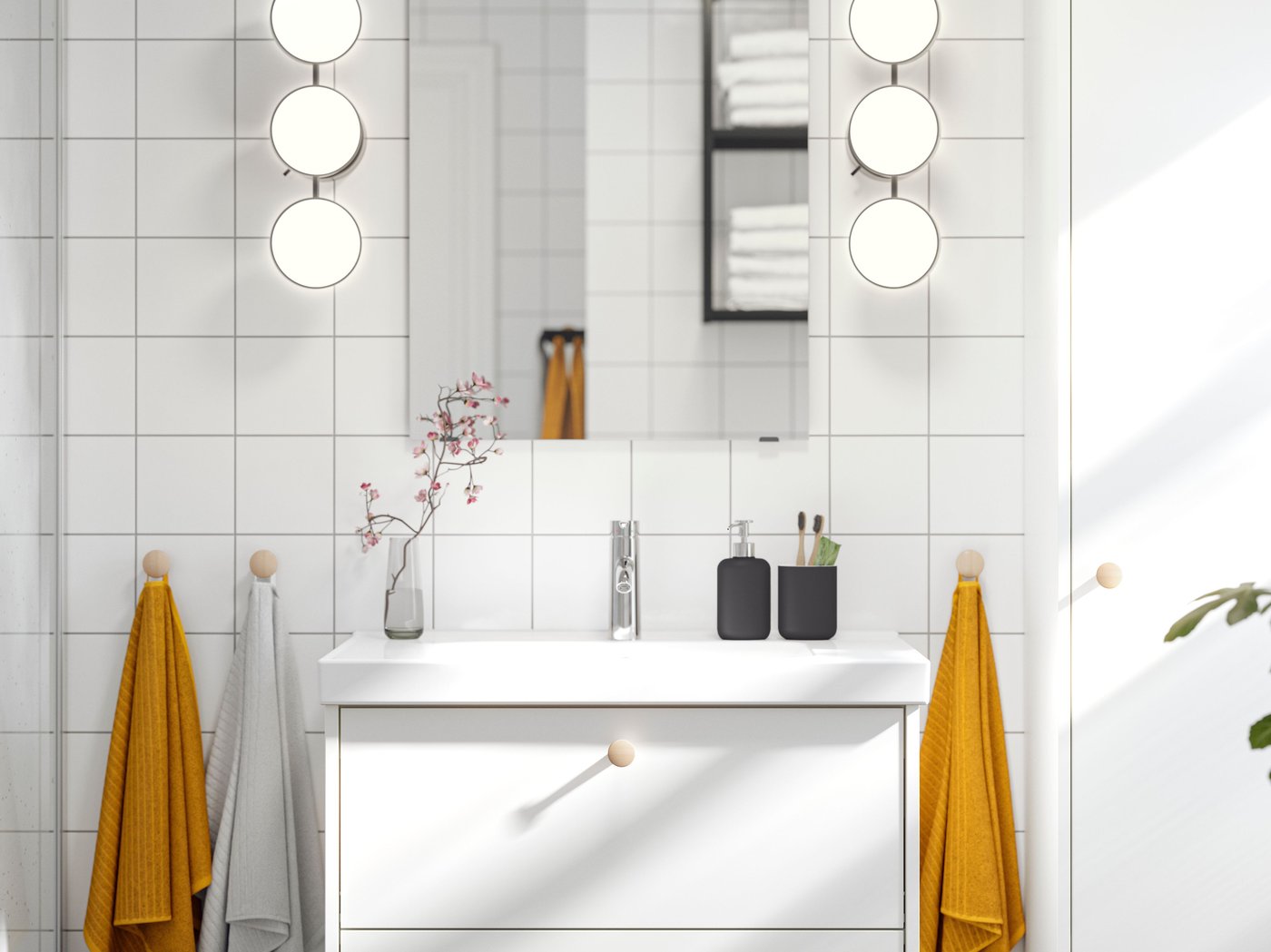 A LETTAN mirror with KABOMBA LED wall lamps on either side of it is placed above a white HAVBÄCK vanity with two drawers.
